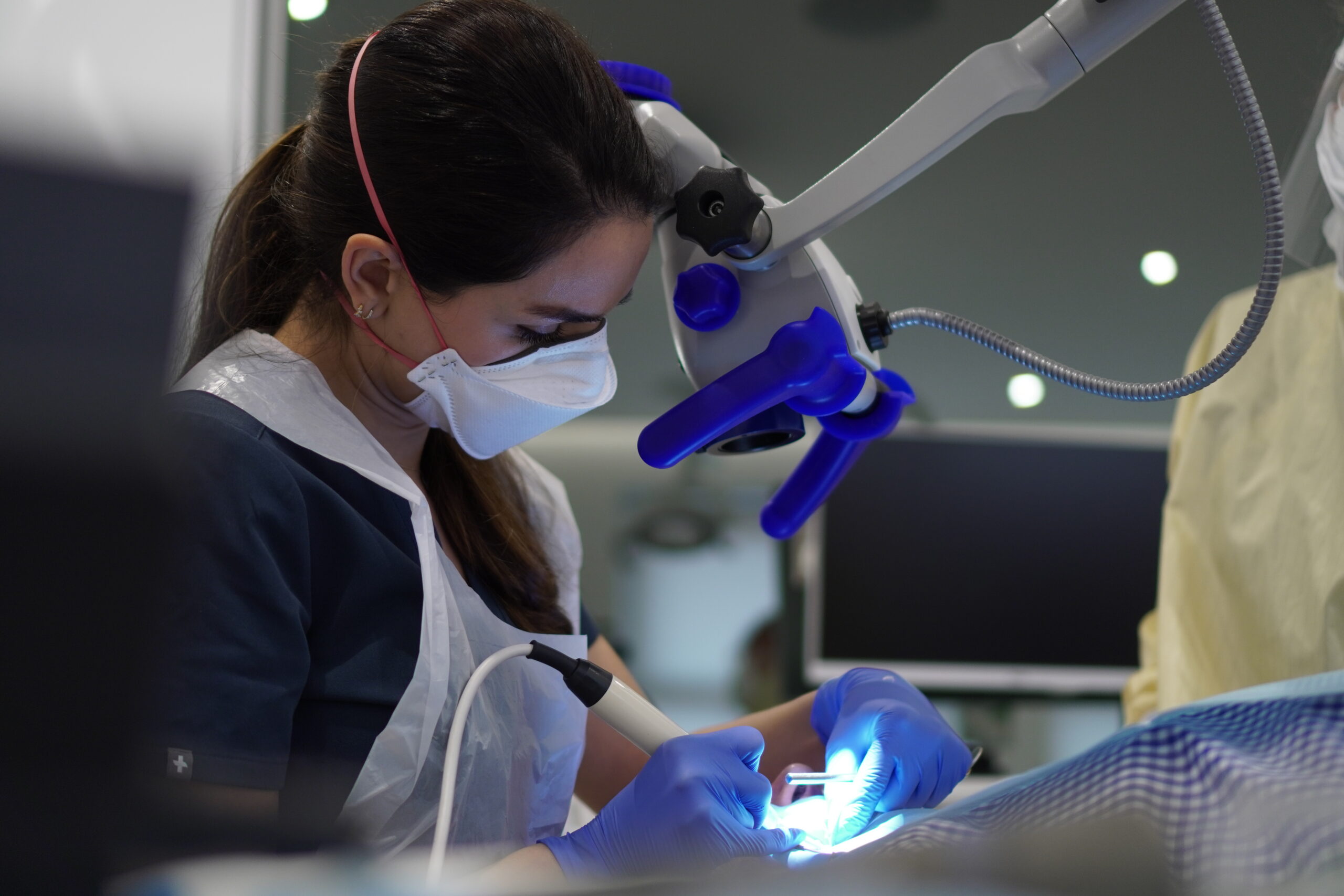A dental professional wearing a mask and gloves uses an illuminated microscope and dental tools to examine a patient’s mouth during a root canal in Hampstead.